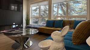 A modern living room with a fireplace, large windows, a sofa with patterned cushions, and a decorative rabbit sculpture.