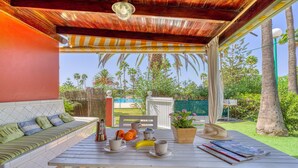 A covered patio with a wooden bench, a table with cups, a banana, and a magazine. - Bungalow in Maspalomas near Golf & Beach (San Bartolomé de Tirajana)