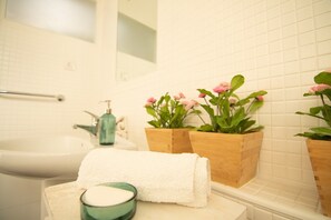 Une salle de bain avec un lavabo blanc, une serviette, un porte-savon et deux jardinières en bois ornées de fleurs roses.