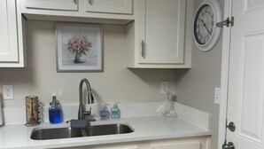 A kitchen with white cabinets, a stainless steel sink, a clock, and a framed picture above the sink. - LED Lighting Reclining Sofas - Cozy 3 Bedroom Home In Jacksonville fl (Jacksonville)