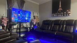 A modern living room with a large flat-screen TV, a black leather sofa, and a wall-mounted Eiffel Tower painting. - LED Lighting Reclining Sofas - Cozy 3 Bedroom Home In Jacksonville fl (Jacksonville)