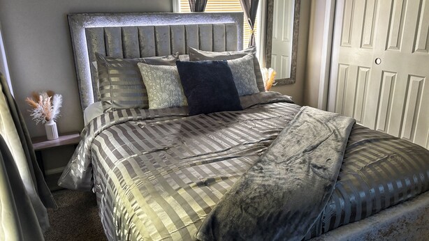 A neatly made bed with striped bedding and a headboard, a bedside table with a vase of dried flowers, and a door with a mirror. - LED Lighting Reclining Sofas - Cozy 3 Bedroom Home In Jacksonville fl (Jacksonville)