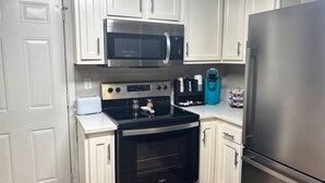 A kitchen with white cabinets, a stainless steel refrigerator, a microwave, a stove, and a coffee maker. - LED Lighting Reclining Sofas - Cozy 3 Bedroom Home In Jacksonville fl (Jacksonville)