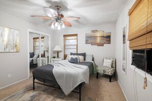 Un dormitorio con cama, una silla, ventilador de techo y obras de arte en las paredes.