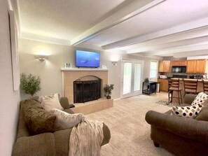 A living room with a fireplace, a television, and a kitchen in the background.