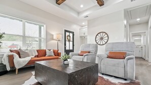 Un salon moderne comprenant un canapé, deux fauteuils, une table basse et une grande fenêtre équipée de stores.