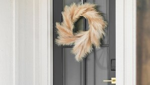 Une porte noire ornée d’une couronne de couleur beige.