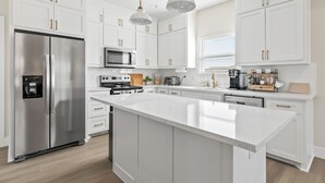 Une cuisine moderne avec des meubles blancs, des appareils en acier inoxydable et des luminaires suspendus.