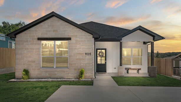 Une maison moderne à deux étages, avec une façade en pierre, le numéro 905, et un porche à l’avant.