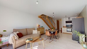 A modern living space with a sofa, coffee table, dining area, kitchen, and a staircase.