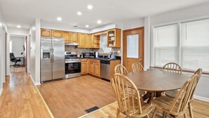 A modern kitchen with wooden cabinets, stainless steel appliances, and a dining area with a wooden table and chairs.