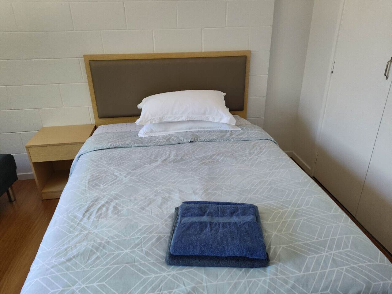 Un lit simple avec une couvre-lit à motifs, une serviette pliée et un oreiller blanc.