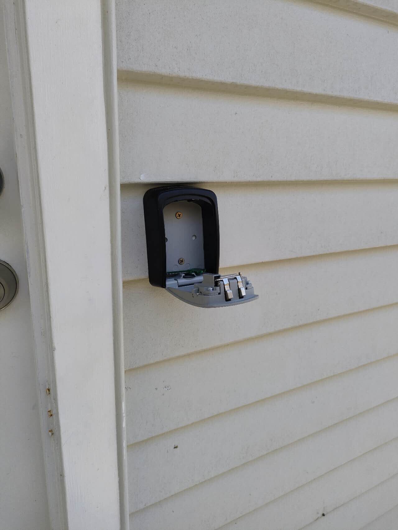 A white exterior wall with a black electrical box and a metal bracket.
