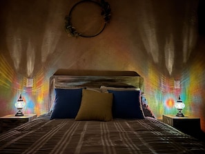 Una cama con una colcha estampada, dos almohadas y un cabecero. A cada lado de la cama hay dos mesitas de noche con lámparas.