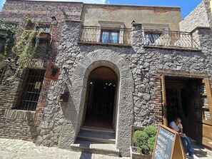 A stone building with an arched entrance, a balcony with metal railings, and a signboard outside. - Loft Belterra (Val'Quirico)