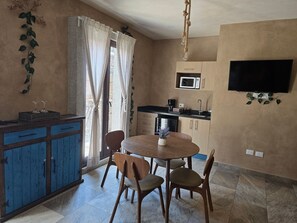 A compact kitchen with a dining area, a TV mounted on the wall, and a window with curtains. - Loft Belterra (Val'Quirico)