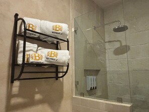 A bathroom with a glass shower enclosure and a towel rack holding two towels with a logo.