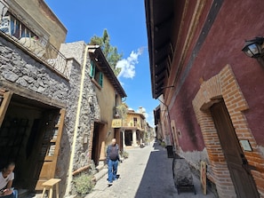 Una estrecha calle empedrada flanqueada por edificios históricos, incluyendo un frente de piedra y una construcción de ladrillo con una puerta de madera.