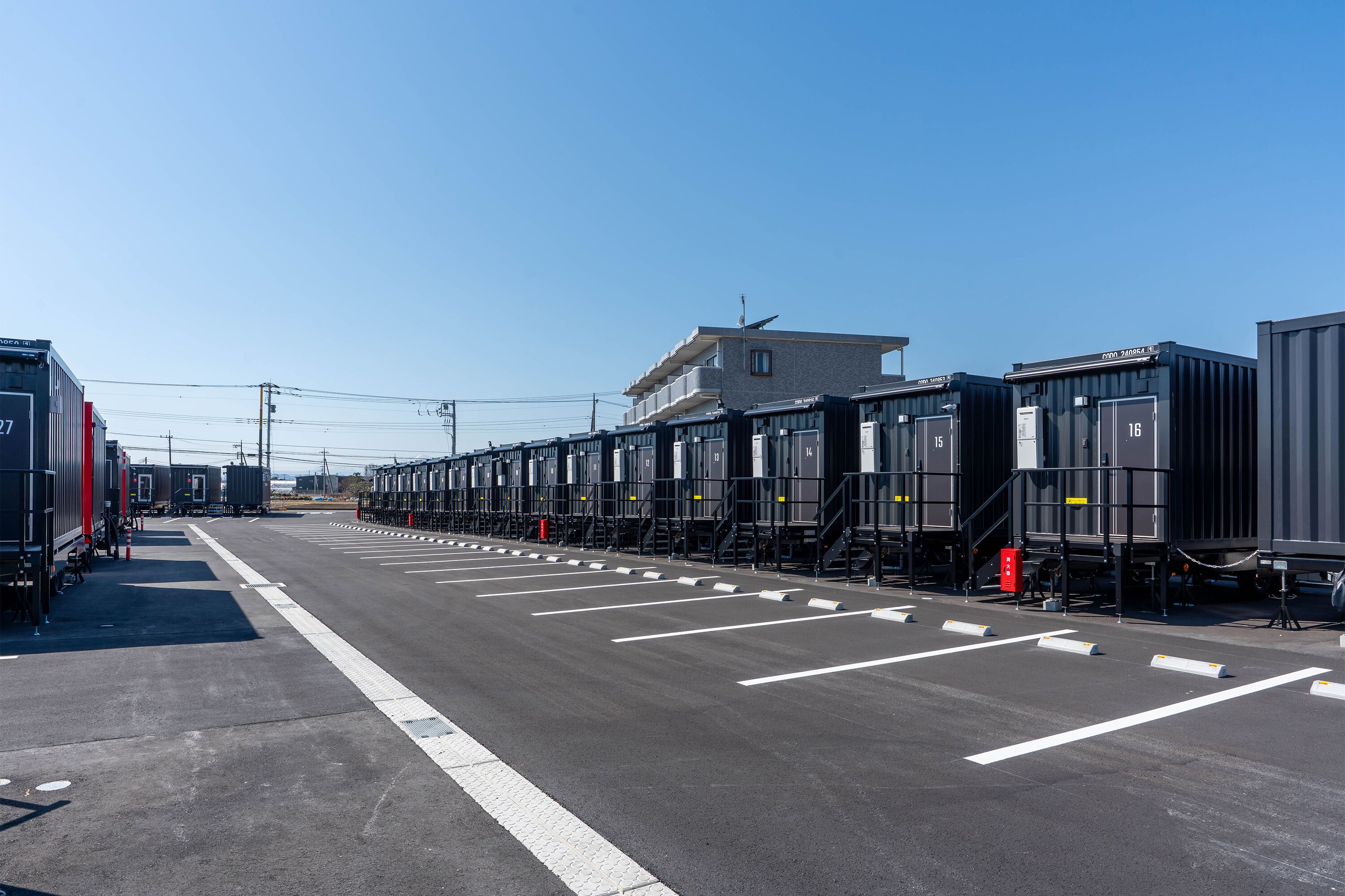 A row of shipping containers arranged in a parking lot with a clear sky above.