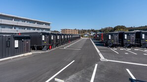 A parking lot with rows of portable cabins, a building with multiple floors, and a clear blue sky. - HOTEL R9 The Yard Otawara (Otawara)