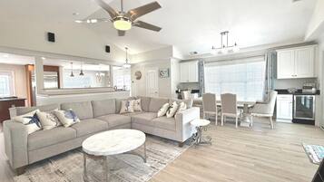 A spacious living room with a sectional sofa, a round coffee table, and a dining area with a table and chairs.