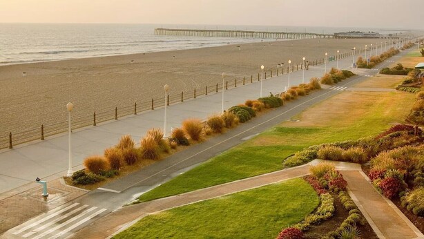 A coastal promenade with a long pier extending into the sea, a pedestrian path alongside, and a grassy area with a fence. - Your Perfect Beach Getaway!  Gorgeous and spacious home perfect for a group! (Virginia Beach)