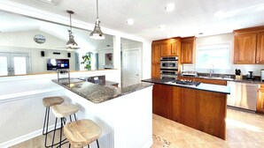 A modern kitchen with a large island, wooden cabinets, stainless steel appliances, and a bar area with stools. - Your Perfect Beach Getaway!  Gorgeous and spacious home perfect for a group! (Virginia Beach)