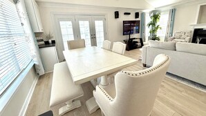 A modern living room with a sofa, a dining table with chairs, a TV, and a fireplace. - Your Perfect Beach Getaway!  Gorgeous and spacious home perfect for a group! (Virginia Beach)