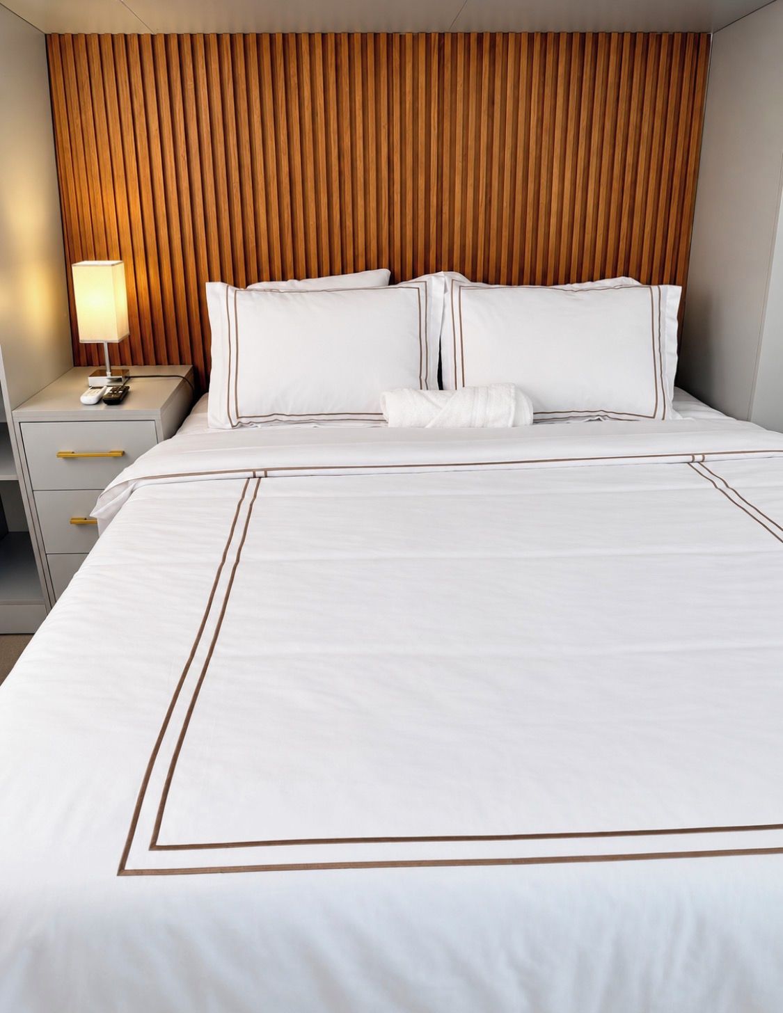 Una camera d'hotel con un letto, un comodino, una lampada e una testiera in legno.