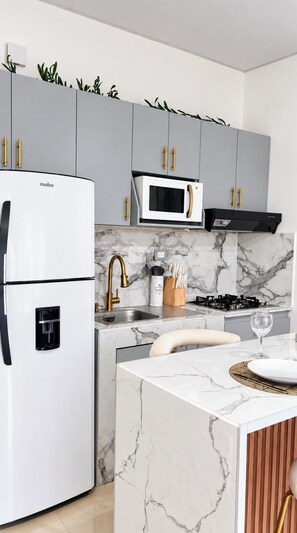 A modern kitchen with grey cabinets, a white refrigerator, a microwave, and a gas stove.
