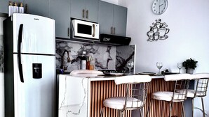 Cozinha moderna com geladeira embutida, micro-ondas e fogão. Há dois banquetas e um relógio na parede.