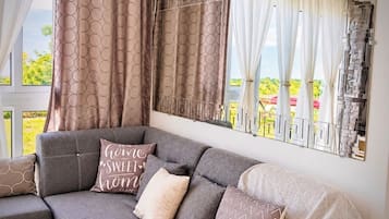 A modern living room with a grey sectional sofa, patterned cushions, and a large window with decorative curtains.