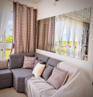 A modern living room with a grey sectional sofa, patterned cushions, and a large window with decorative curtains. - Tu refugio a pasos de centros Comerciales (San Miguel)