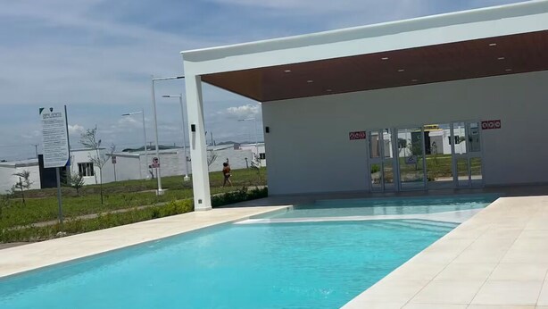 Uma piscina com água azul cristalina, área coberta com porta e vista para o mar ao fundo.
