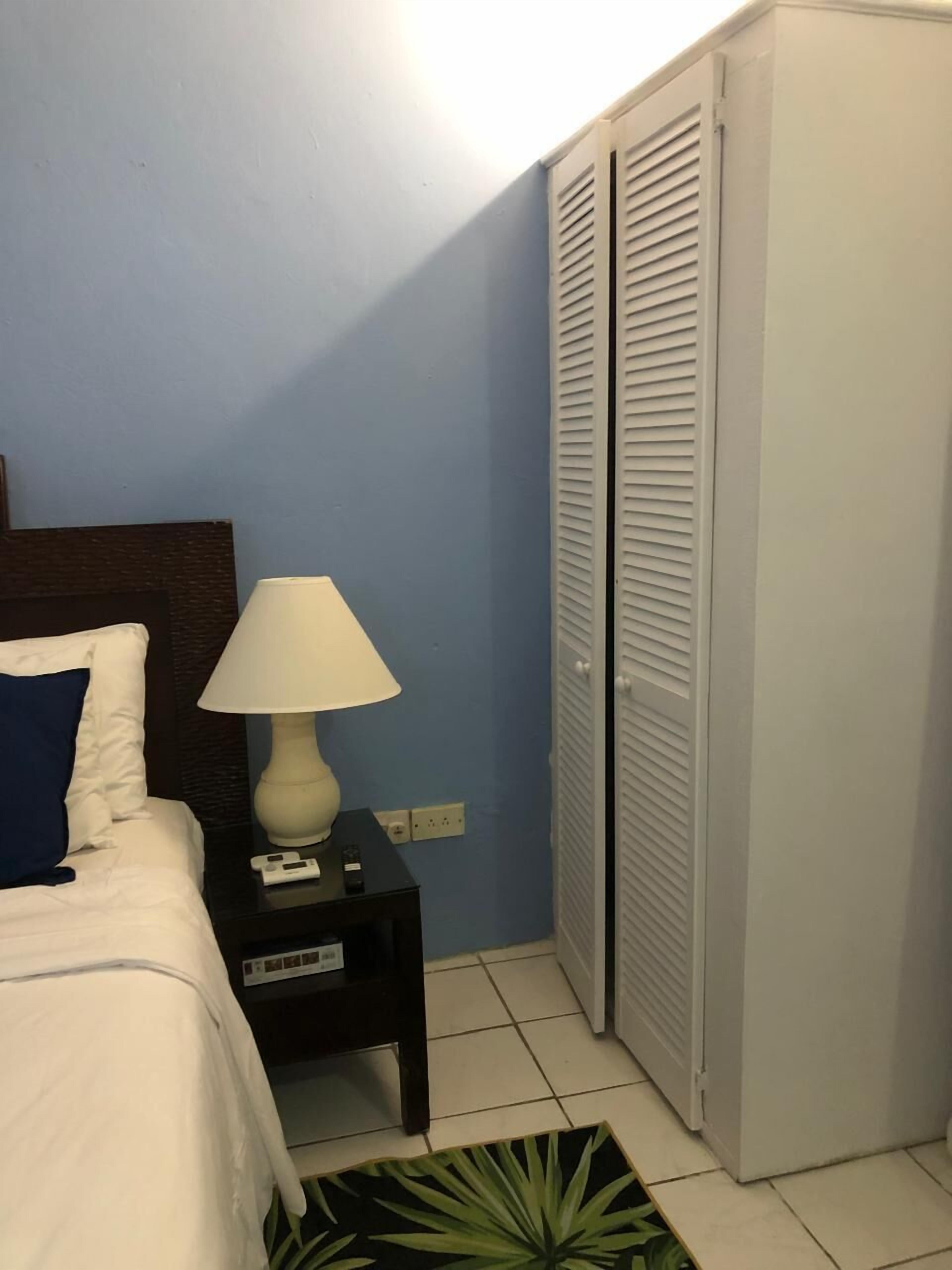 A bedroom with a bed, a bedside table with a lamp, a nightstand, and a wardrobe.
