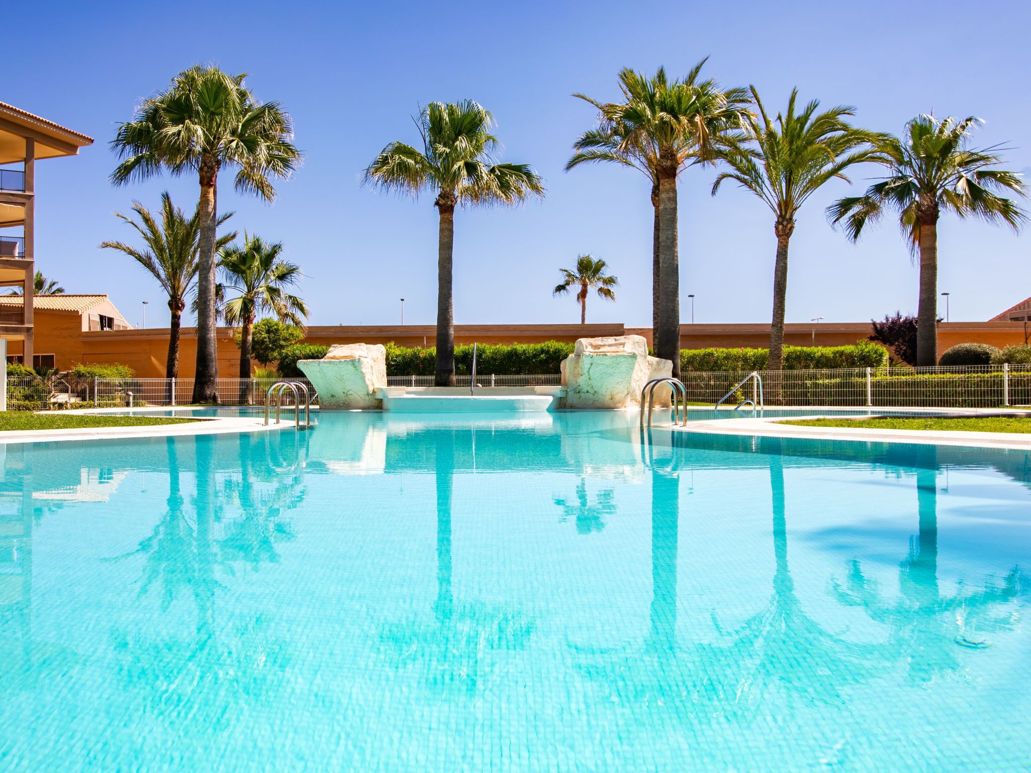 A clear blue pool with palm trees and a building in the background.