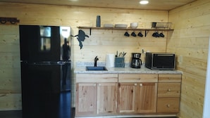 Una cocina con armarios de madera, un refrigerador negro, una cafetera y un microondas.