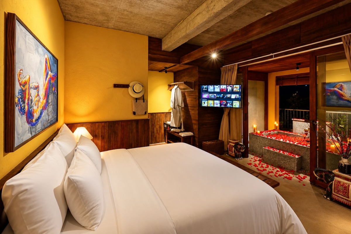 A hotel room with a bed, artwork, a television, and a balcony with red flowers.