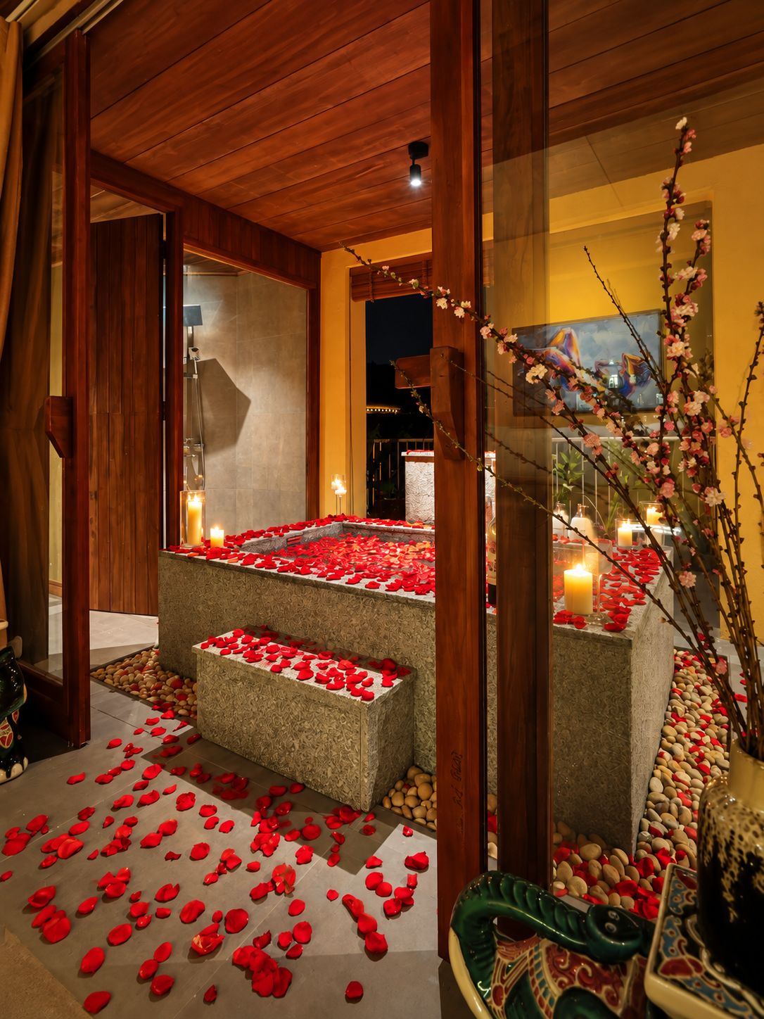 A serene indoor setting with a stone bench surrounded by rose petals and candles, suggesting a romantic or intimate atmosphere.