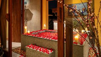 A serene indoor setting with a stone bench surrounded by rose petals and candles, suggesting a romantic or intimate atmosphere.