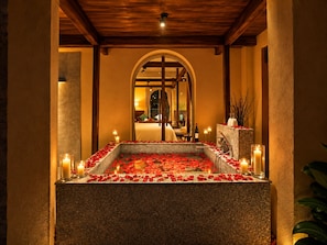 A stone-tiled pool with rose petals and candles, surrounded by pillars and a wooden ceiling. - Nexus House An Son Da Lat (Xuan Huong - Da Lat)