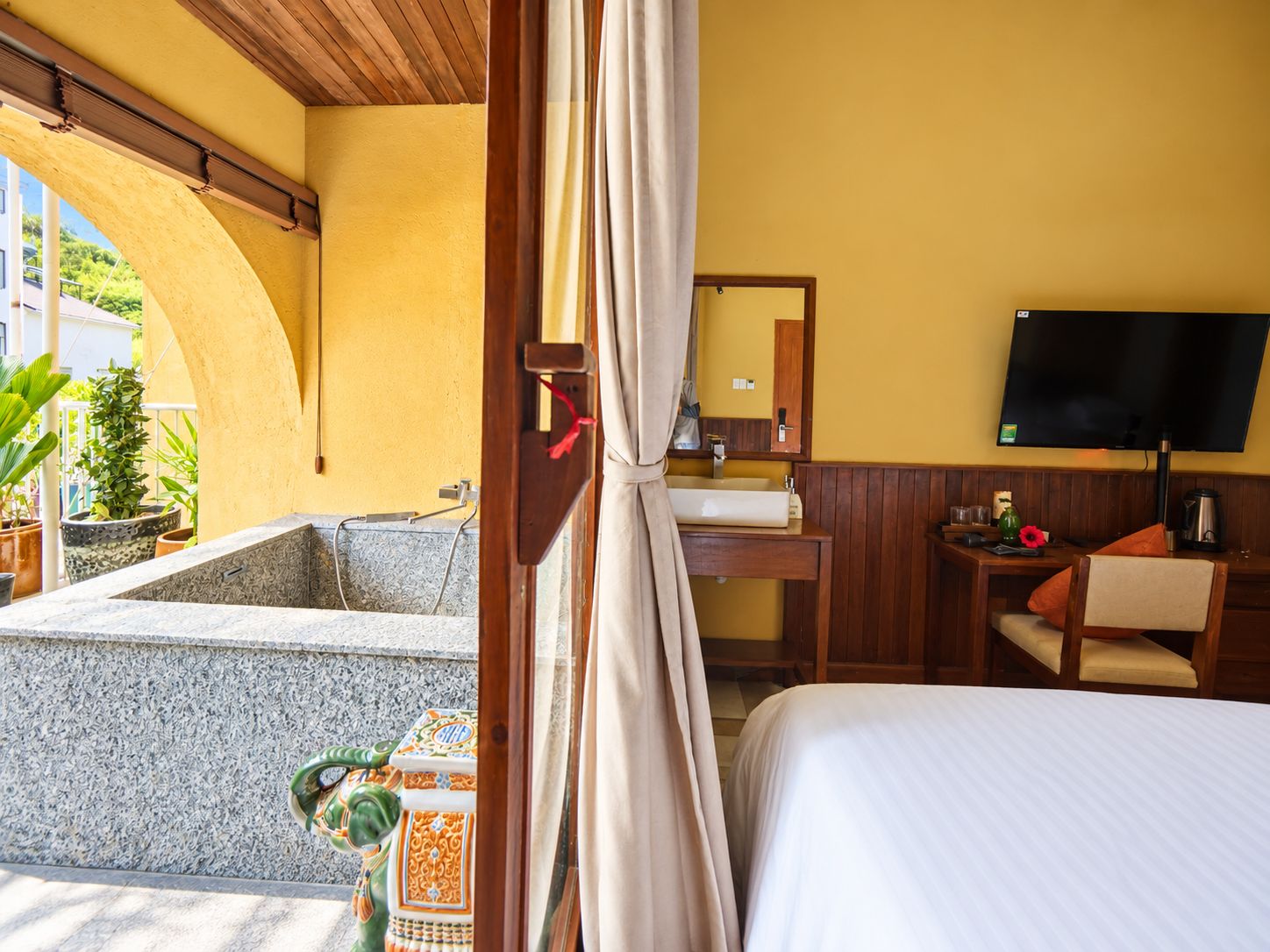 A hotel room with a bed, a desk, a television, a bathroom with a bathtub, and a view of the outside.
