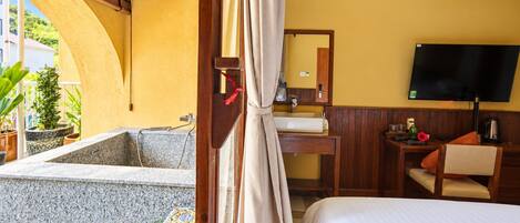 A hotel room with a bed, a desk, a television, a bathroom with a bathtub, and a view of the outside.