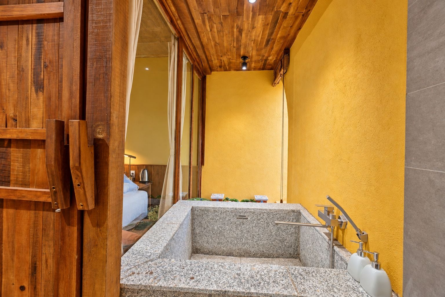 A bathroom with a freestanding bathtub, wooden ceiling, and a yellow wall.