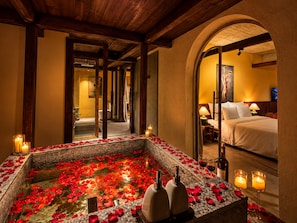 A spa area with a hot tub surrounded by rose petals, candles, and a bed in the background. - Nexus House An Son Da Lat (Xuan Huong - Da Lat)