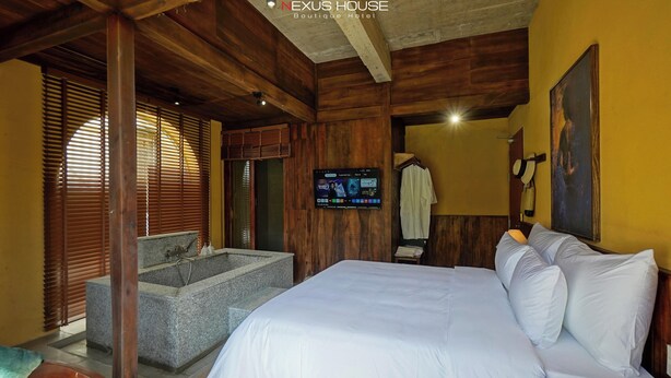 A hotel room with a large bed, a wooden ceiling, a stone bathtub, and a TV on the wall.
