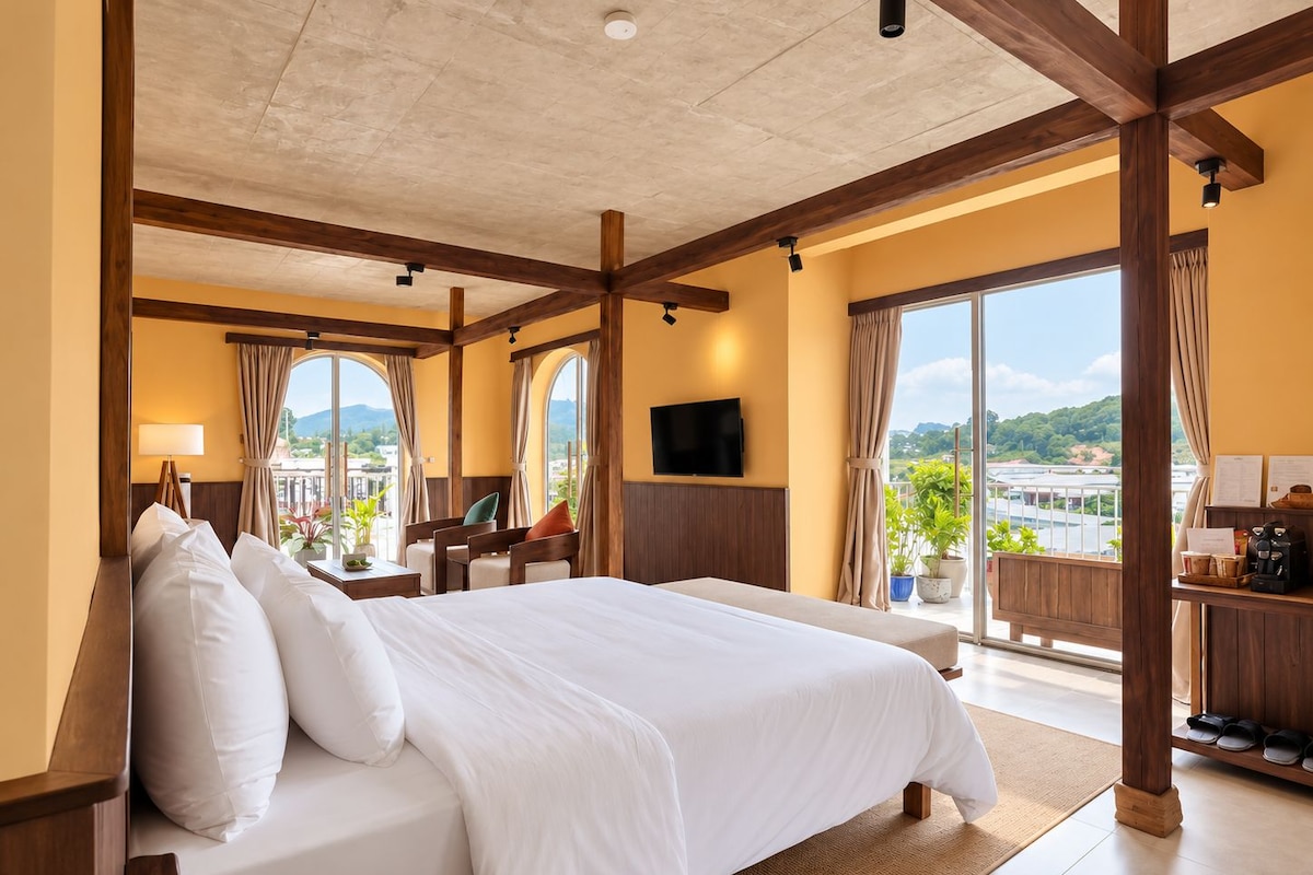 A hotel room with a large bed, a desk, a chair, a TV, and a balcony with a view.