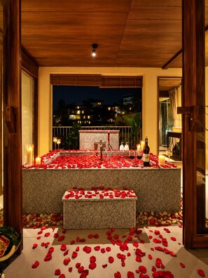 Un cadre romantique en plein air, avec un banc en pierre, des bougies et des pétales de rose.