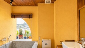 A bathroom with a bathtub, toilet, sink, and shower. There are potted plants on a balcony. - Nexus House An Son Da Lat (Xuan Huong - Da Lat)