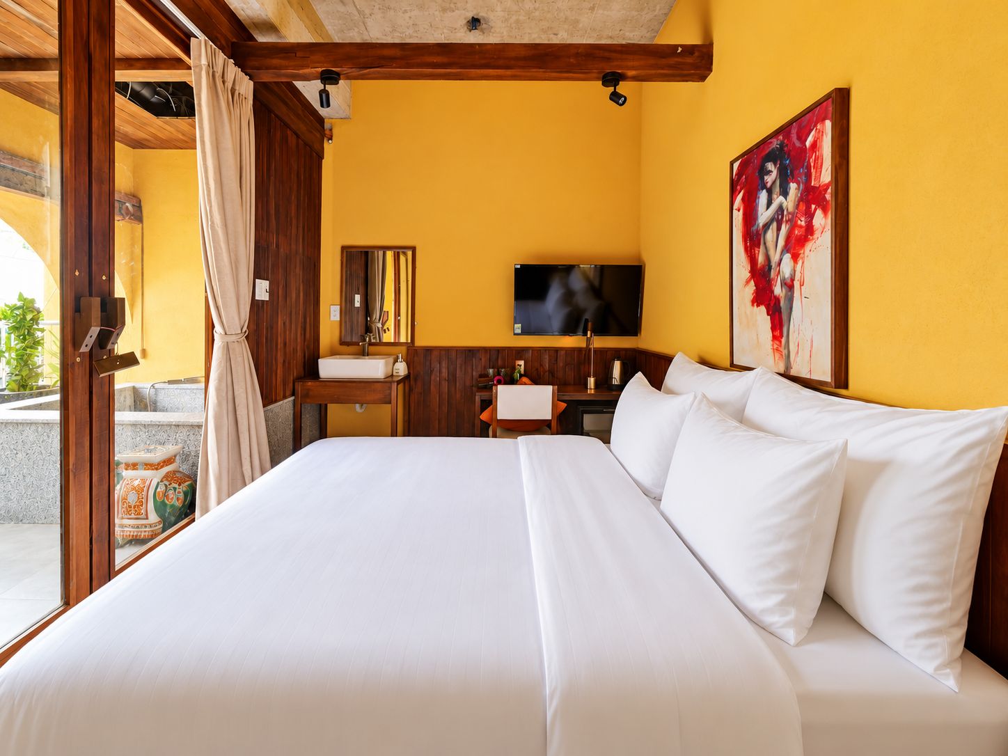 A hotel room with a large bed, a television, a bathroom with a sink, and a painting on the wall.